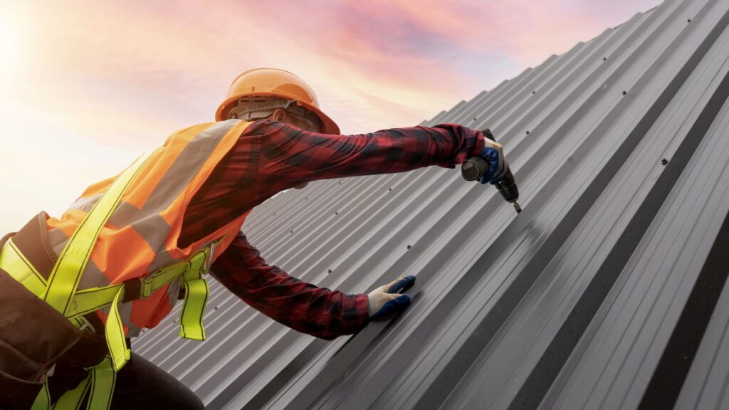 A construction worker in safety gear installs metal roofing panels