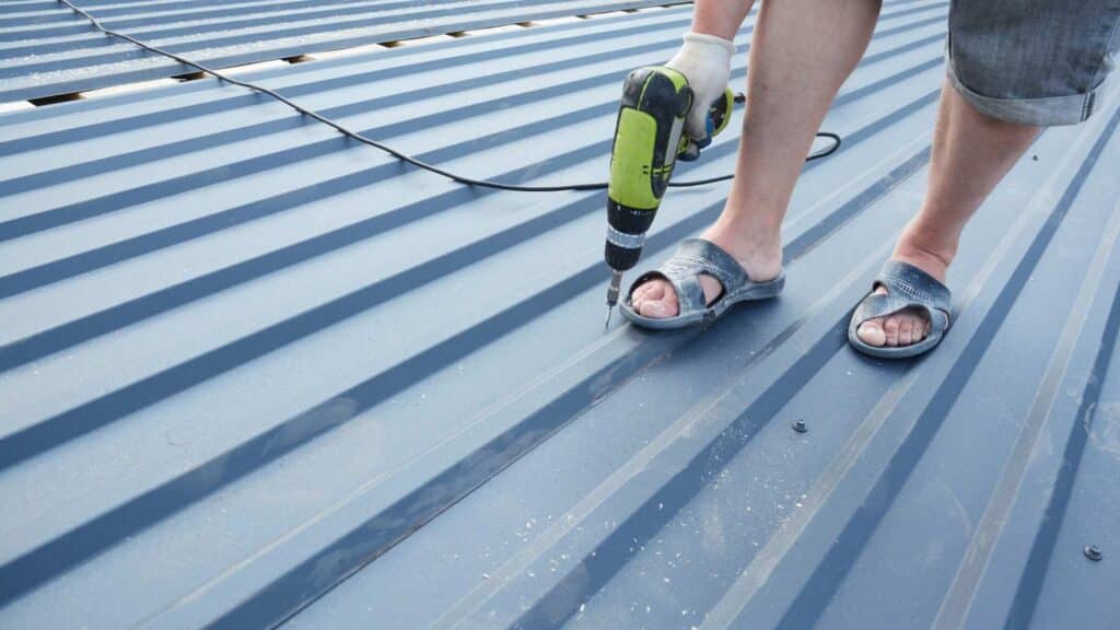 Person using a nail gun to fasten sheet metal to wood as a roof